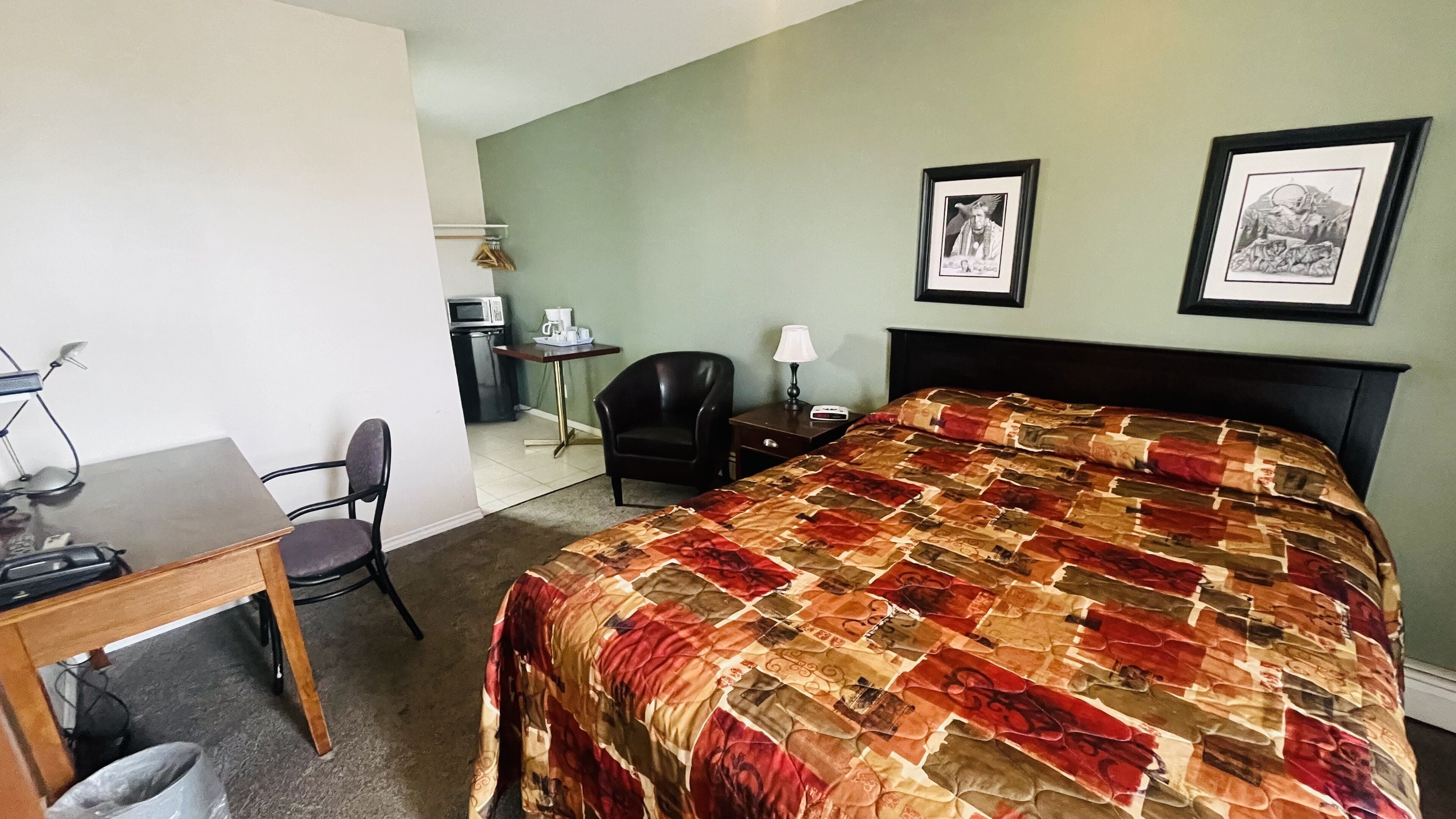 Camera d'albergo con un letto, una scrivania, una sedia, una lampada e due quadri appesi al muro.