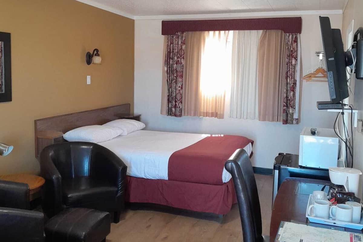 Quarto de hotel com cama, duas cadeiras, escrivaninha com computador e pequena mesa com xícaras.