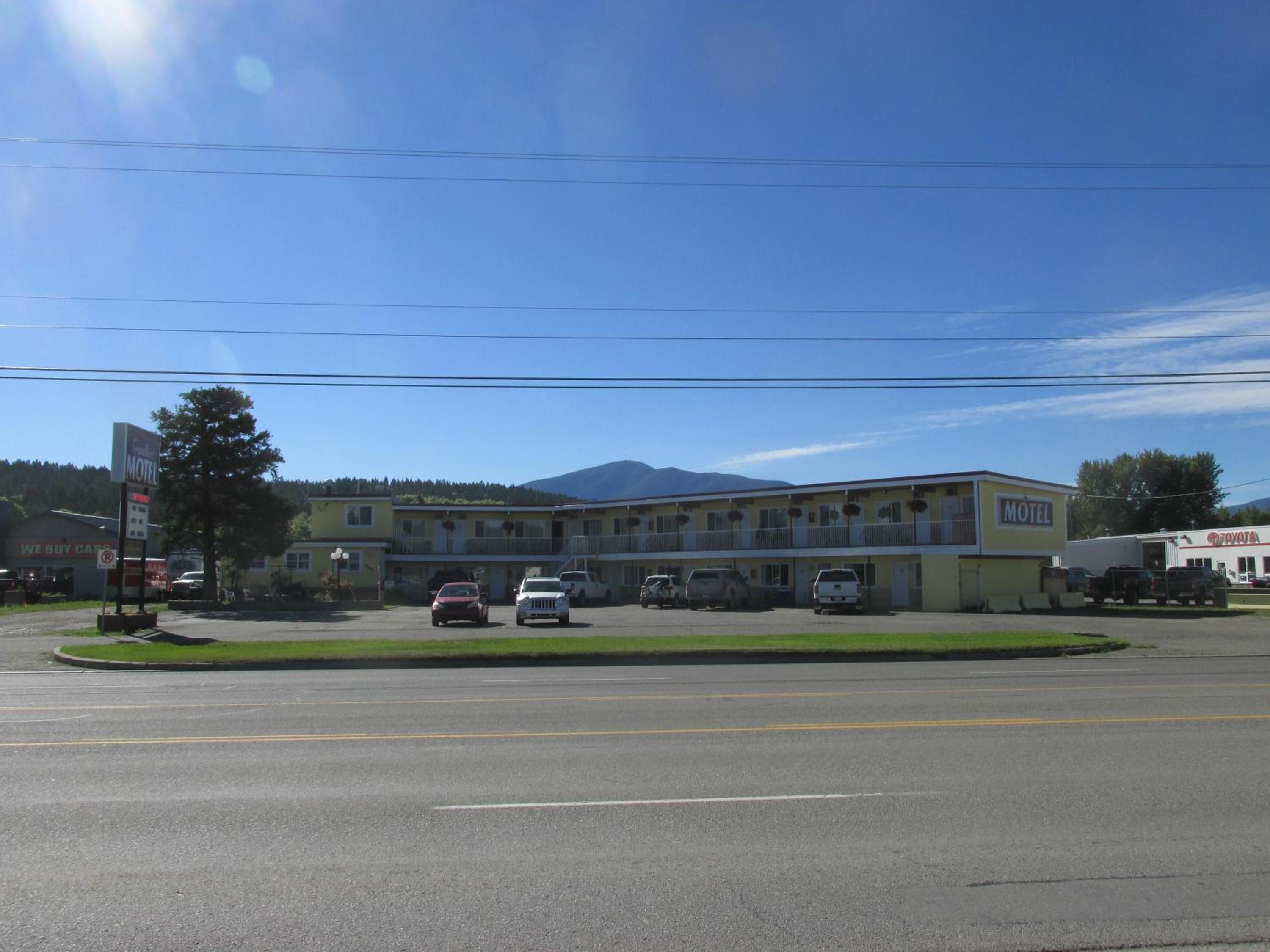 A motel with a parking lot, a building with a yellow facade, and a mountain in the background.