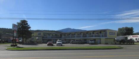 A motel with a parking lot, a building with a yellow facade, and a mountain in the background.