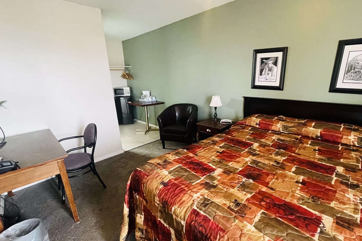 Quarto de hotel com uma cama, uma escrivaninha, uma cadeira, um abajur e duas imagens emolduradas na parede.
