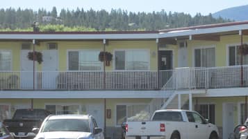 A two-story motel with a yellow facade, a balcony with white railings, and a parking lot with several vehicles.
