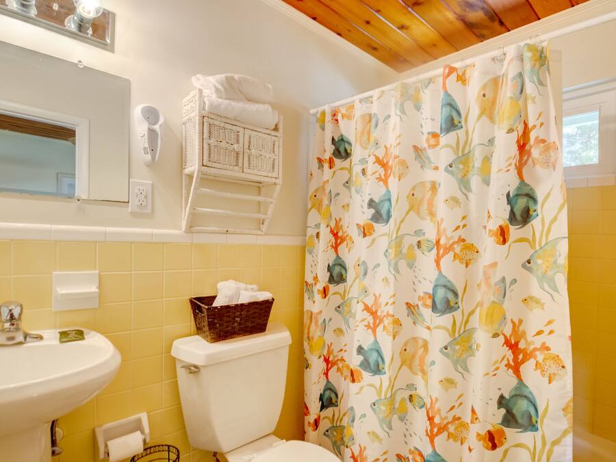 A bathroom with a yellow tiled wall, a white sink, a toilet, a shower curtain with a fish pattern, and a mirror above the sink.