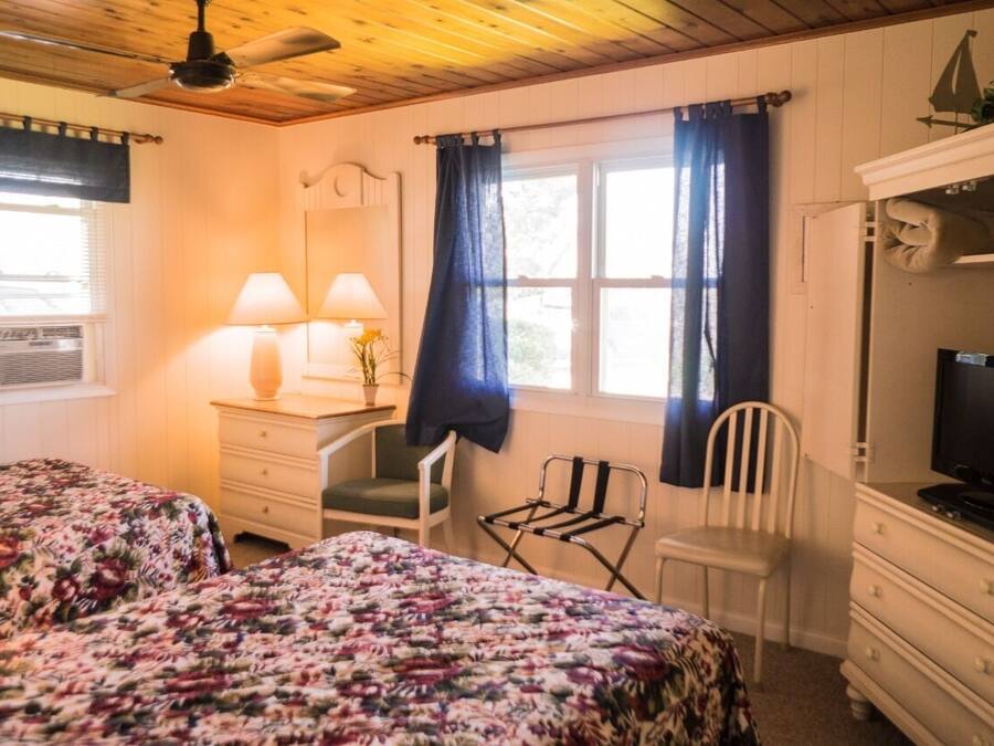 A bedroom with two beds, a desk with a chair, a television, and a window with curtains.