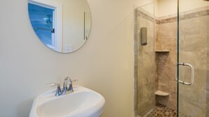 A bathroom with a round mirror, a sink, and a glass-enclosed shower area.