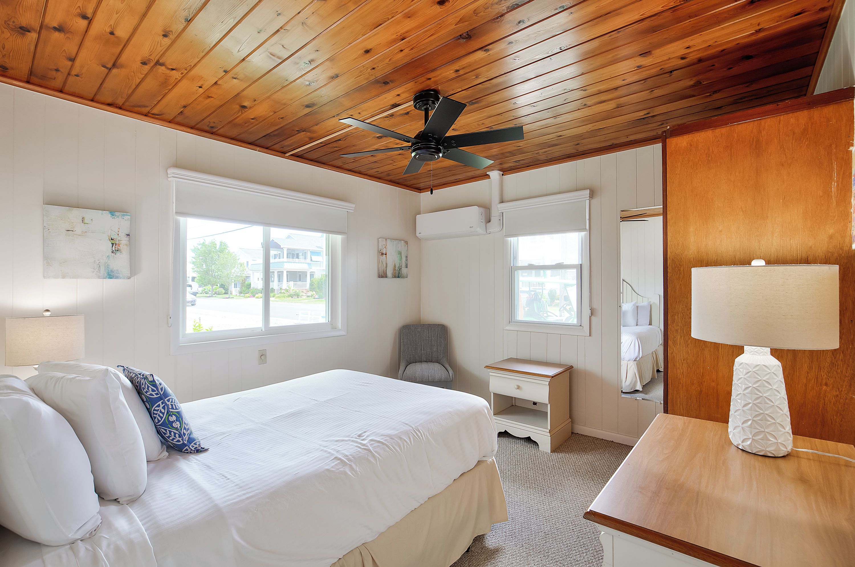 A bedroom with a bed, a desk, a chair, a ceiling fan, and a window.