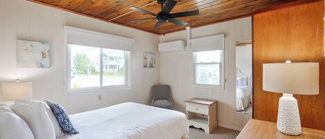 A bedroom with a bed, a desk, a chair, a ceiling fan, and a window.