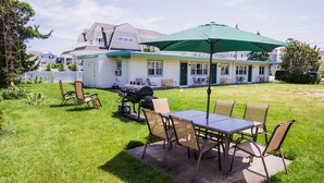 A backyard with a barbecue grill, outdoor table, and chairs, surrounded by a well-maintained lawn and a house in the background.