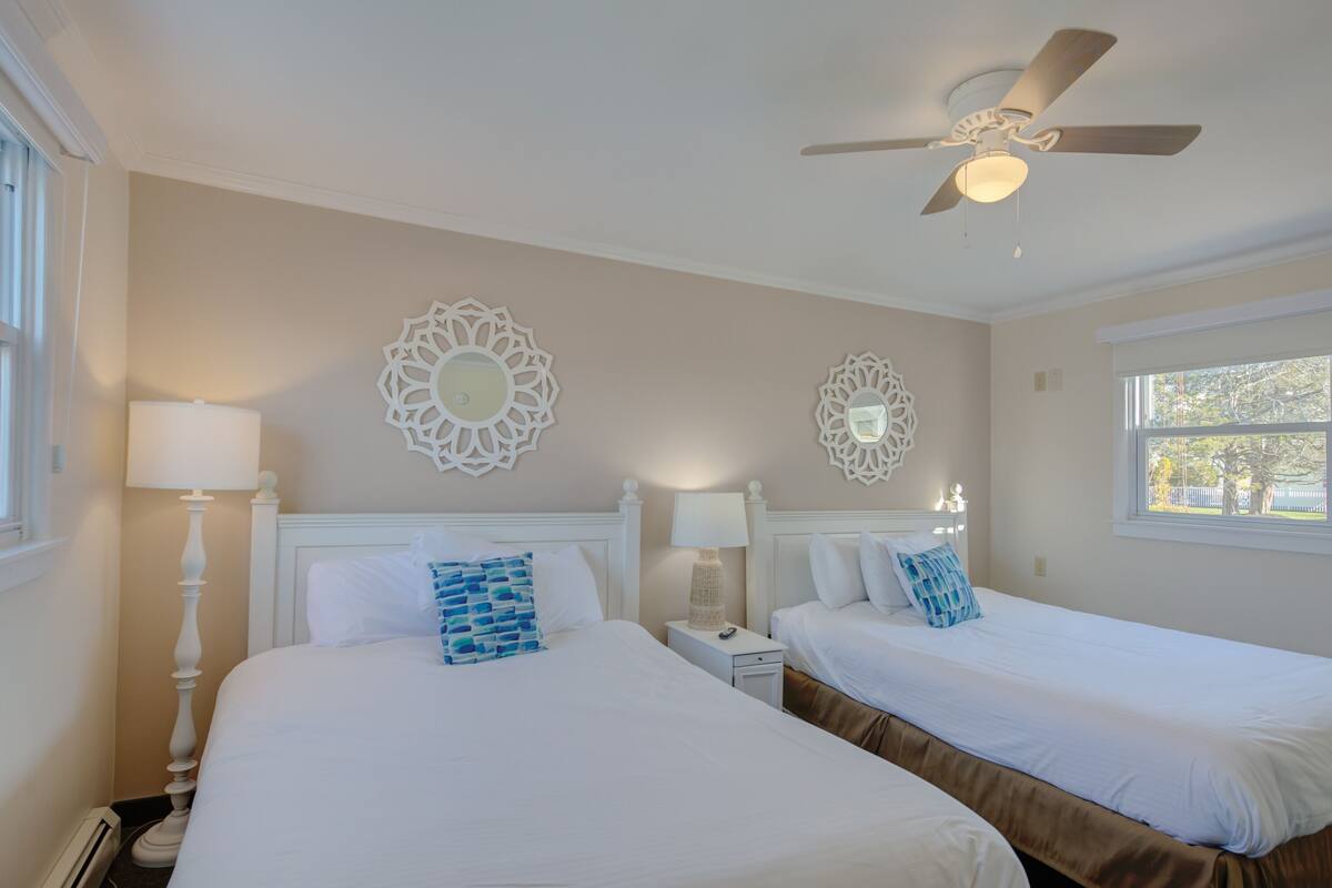 Quarto de hotel com duas camas, um ventilador de teto, arte decorativa na parede e janela com vista.