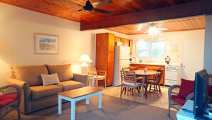 A cozy living room with a sofa, a coffee table, and a dining area with chairs and a table. There is a kitchen with a stove and refrigerator.