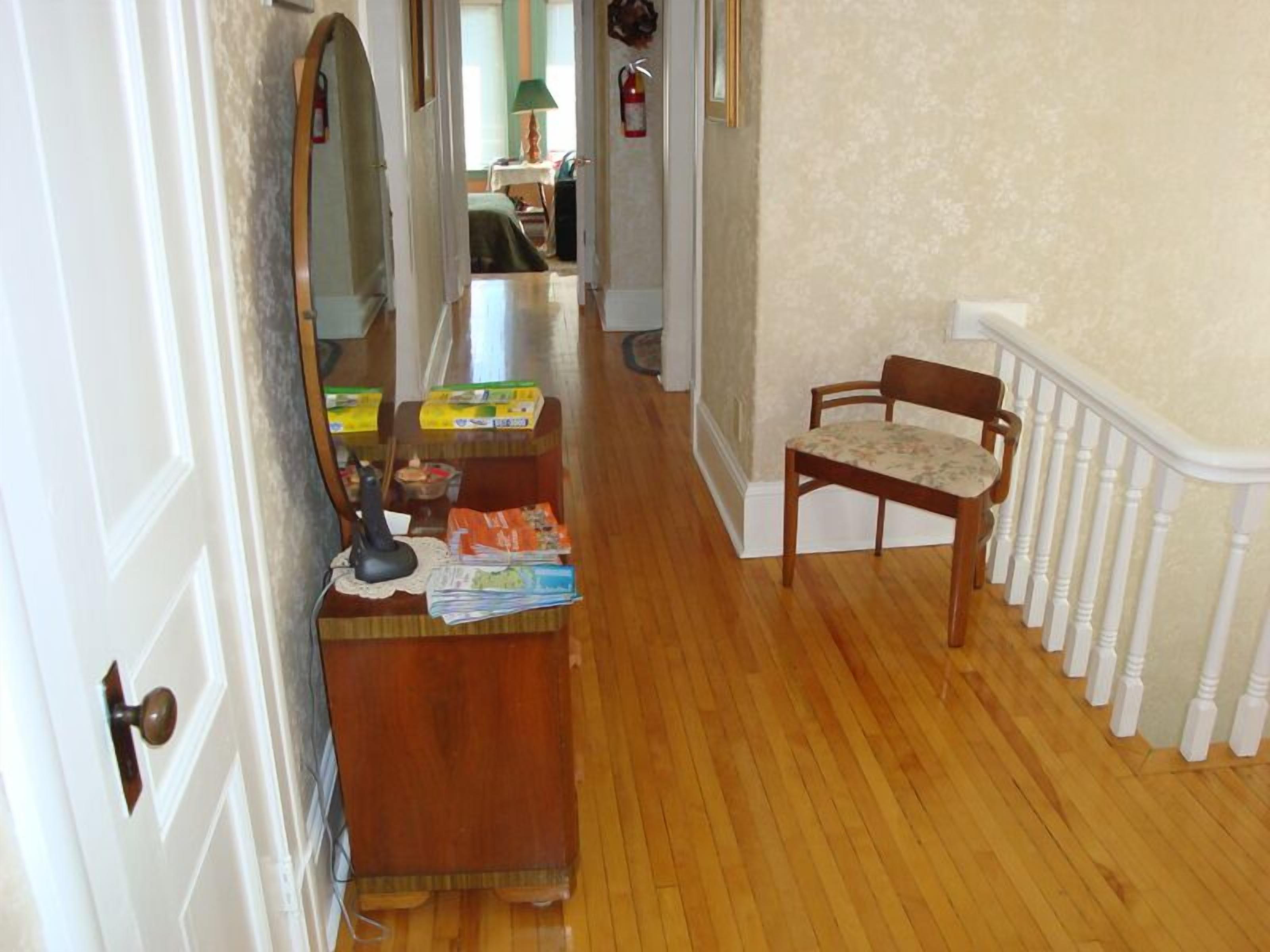 A hallway with a wooden floor, a desk with various items, a chair, and a white railing.