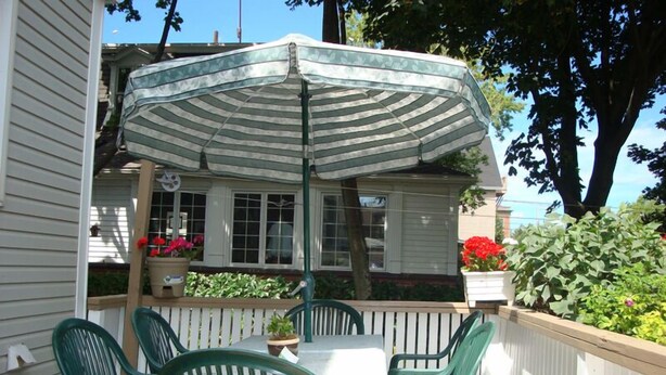 A patio with a table and chairs, a striped umbrella, and potted plants. - Downtown Bed And Breakfast (Moncton)