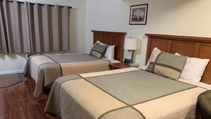 A hotel room with two beds, a wooden headboard, a nightstand with a lamp, and a framed picture on the wall.
