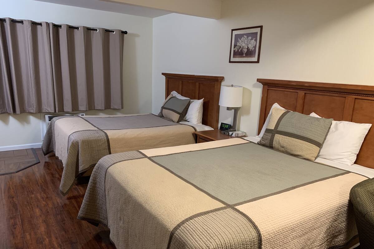 Une chambre d’hôtel avec deux lits, une tête de lit en bois, une table de chevet avec une lampe et un tableau encadré au mur.