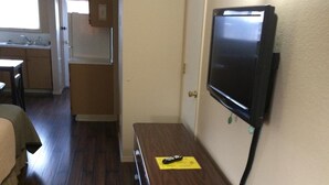 A room with a wooden floor, a television mounted on the wall, a small wooden table, and a door leading to another room.