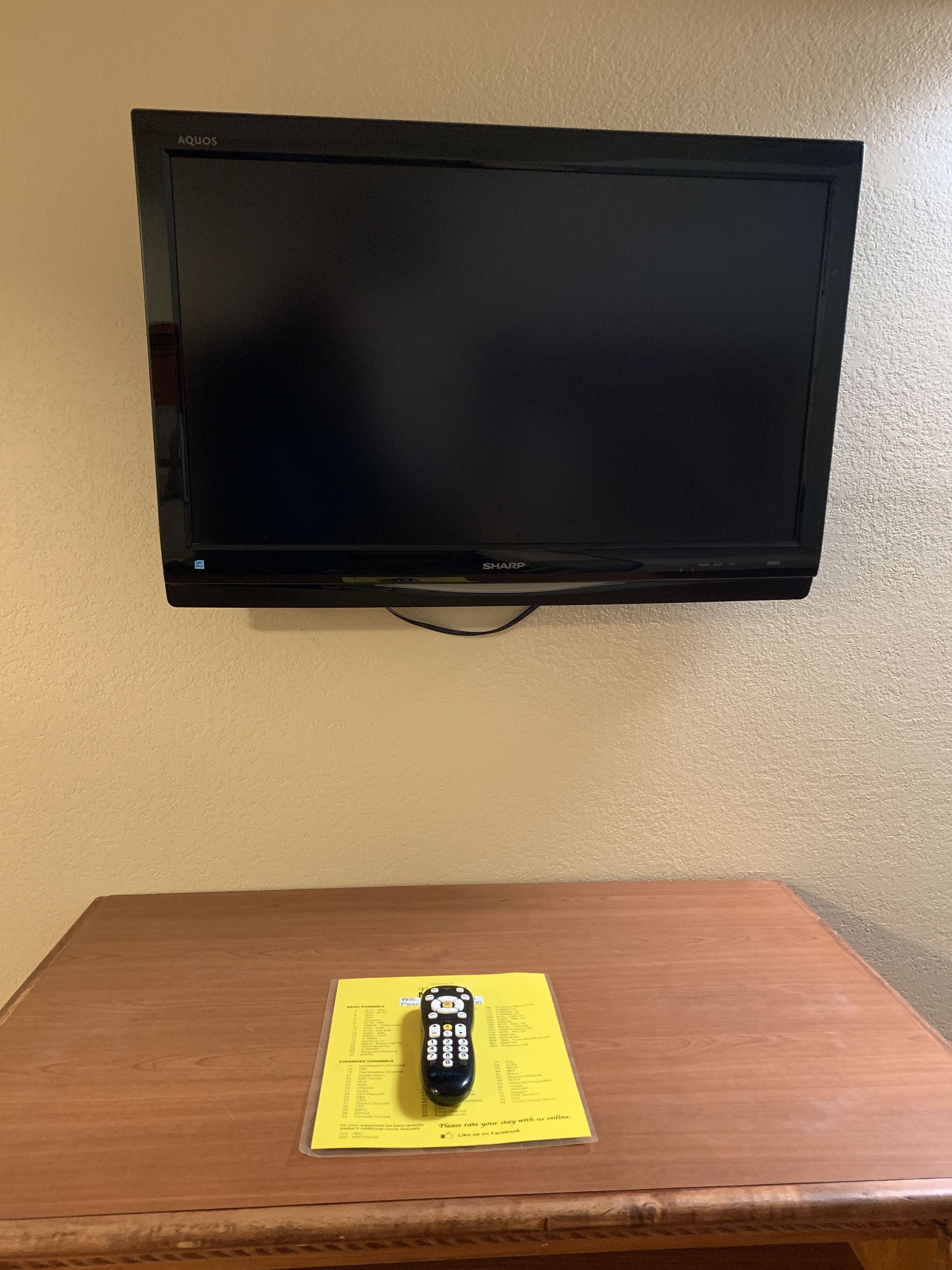 En platt-TV som är monterad på väggen, ett träbord med en fjärrkontroll och ett gult papper under.