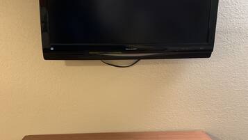 En platt-TV som är monterad på väggen, ett träbord med en fjärrkontroll och ett gult papper under.