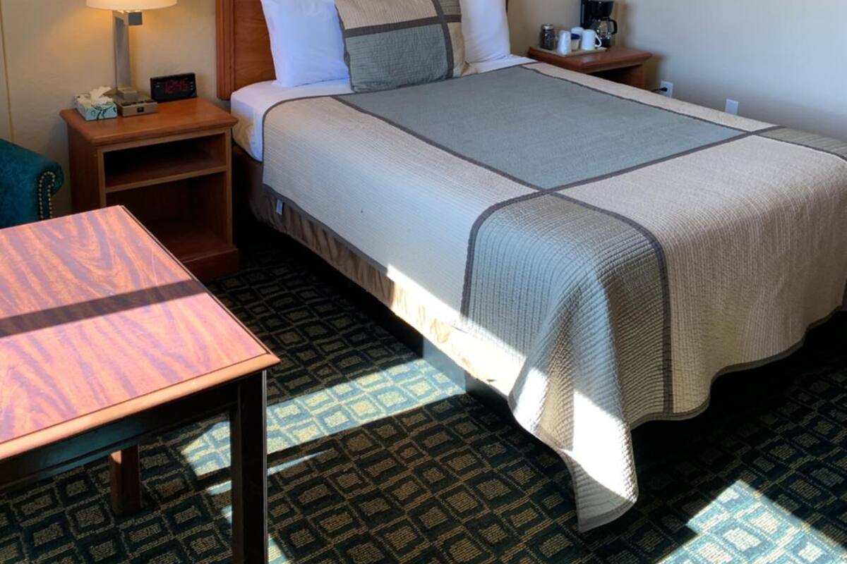 Une chambre d’hôtel avec un lit, une table de chevet avec une lampe, une horloge et un tableau encadré au mur.