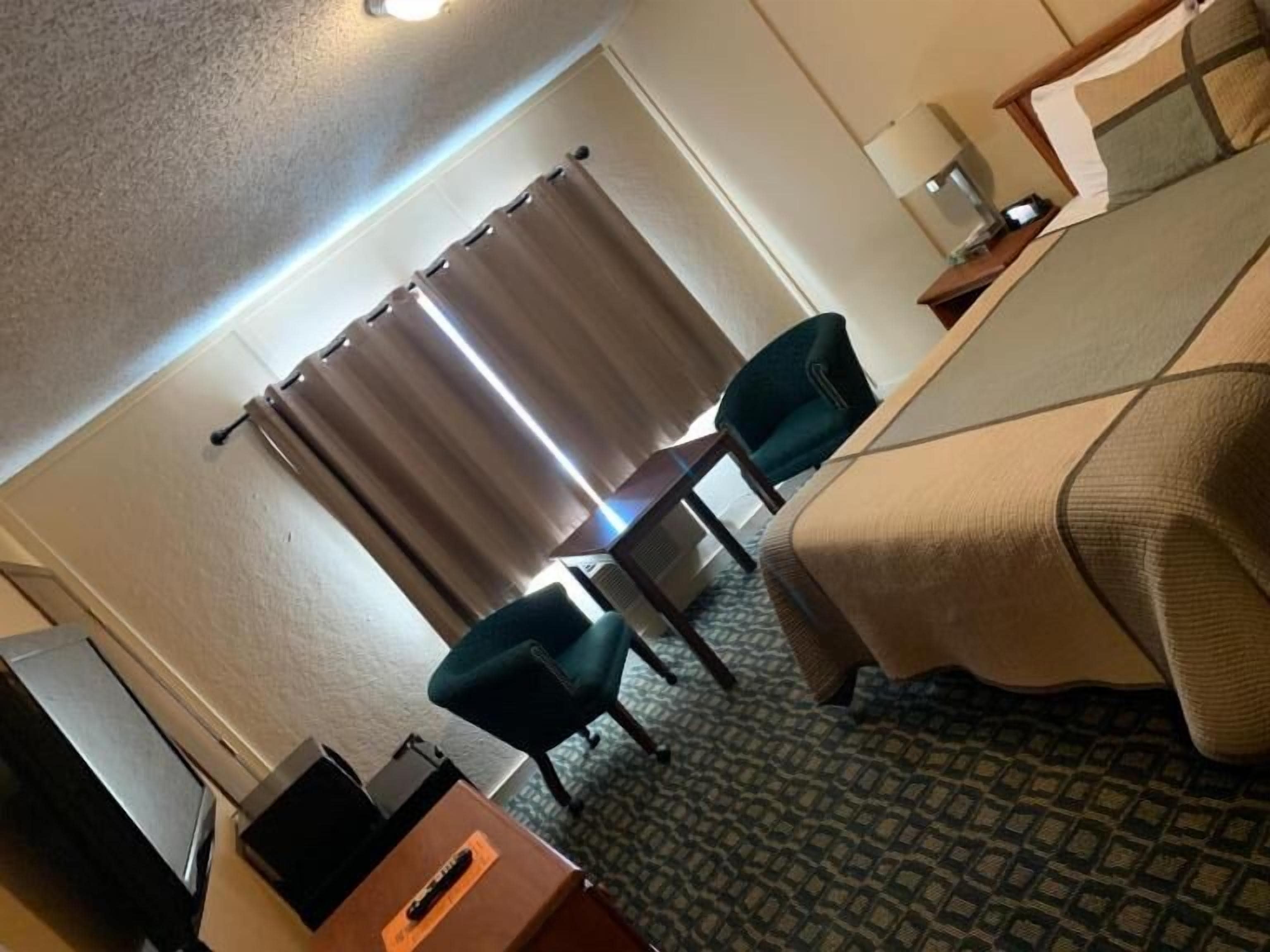 Une chambre d’hôtel avec un lit, un bureau, une chaise et une fenêtre avec des rideaux.