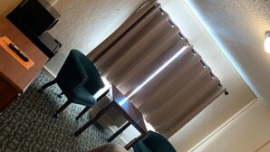 A hotel room with a bed, two chairs, a small table, and a window with curtains.