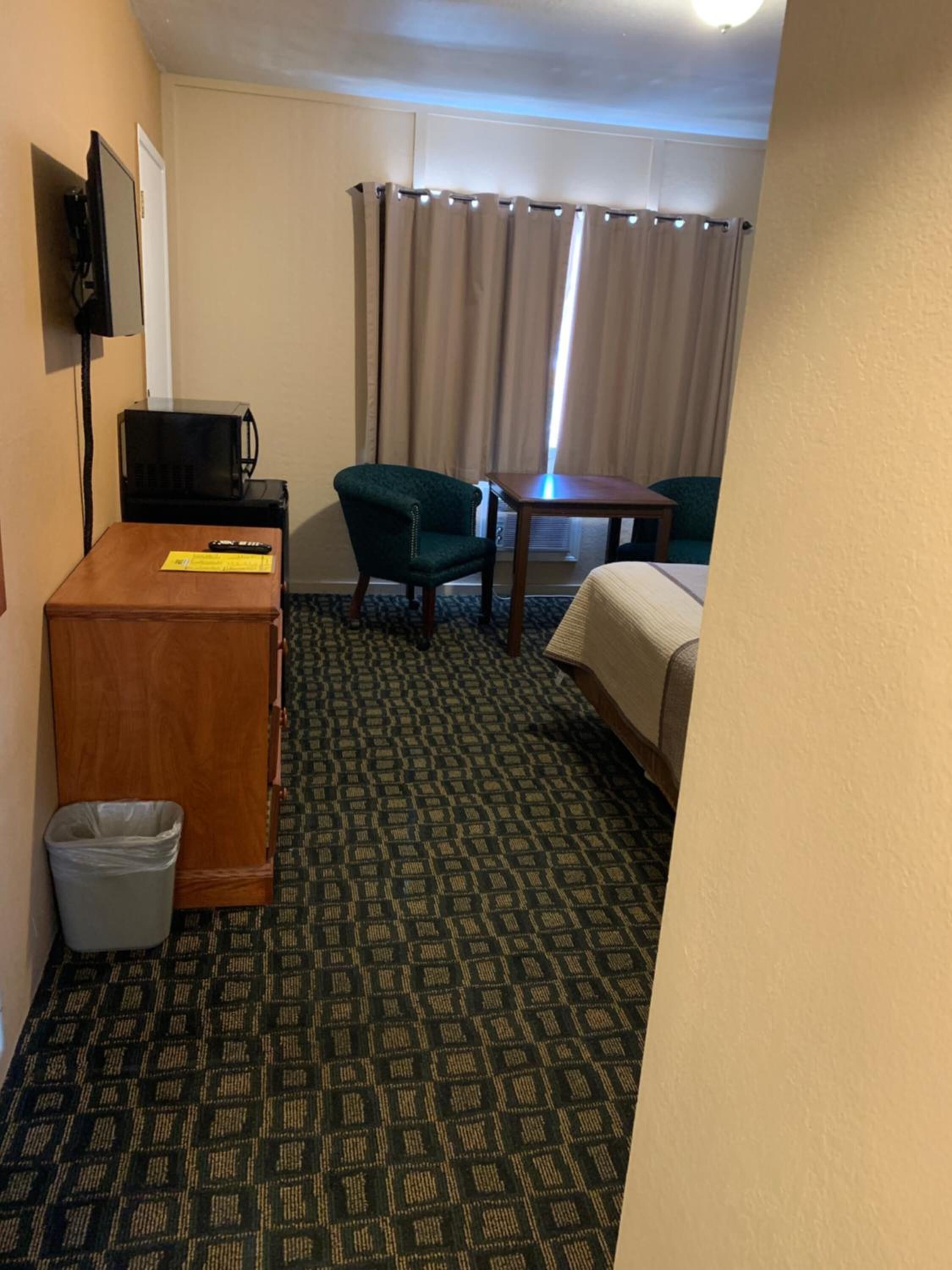 A hotel room with a bed, a desk with a computer, a chair, a small table, a TV, and a trash bin.
