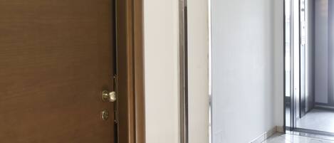 A hotel room with a wooden door, a small window, and a tiled floor.