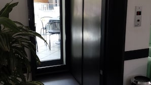 A modern elevator with a digital display, a potted plant, and a view of an outdoor balcony area. - Hotel Penny (Rimini)