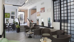 A hotel lobby with wicker furniture, a staircase, and artwork on the walls. - Hotel Penny (Rimini)