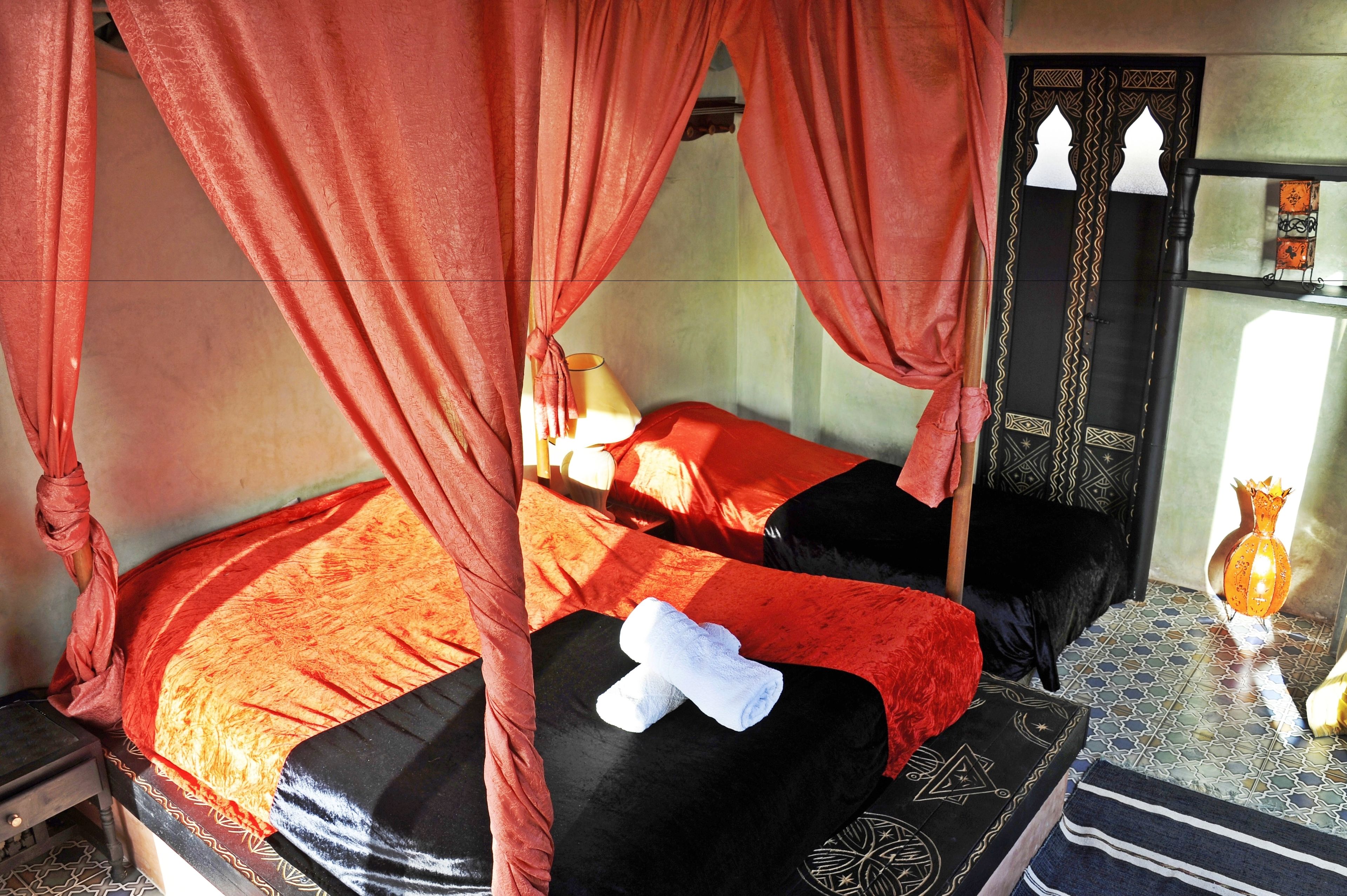 Una habitación con una cama cubierta por cortinas rojas, un edredón rojo y negro, y una toalla blanca sobre la cama.