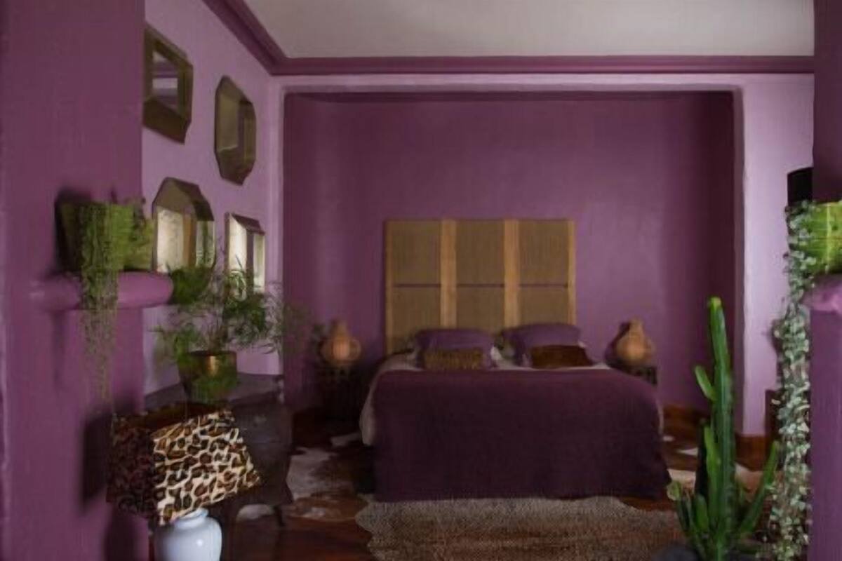 Un dormitorio con una cama grande, paredes moradas y plantas decorativas.