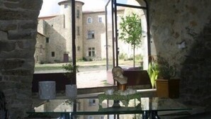Una habitación con pared de piedra, una mesa de vidrio con un florero y una ventana con vista a un edificio con un árbol.
