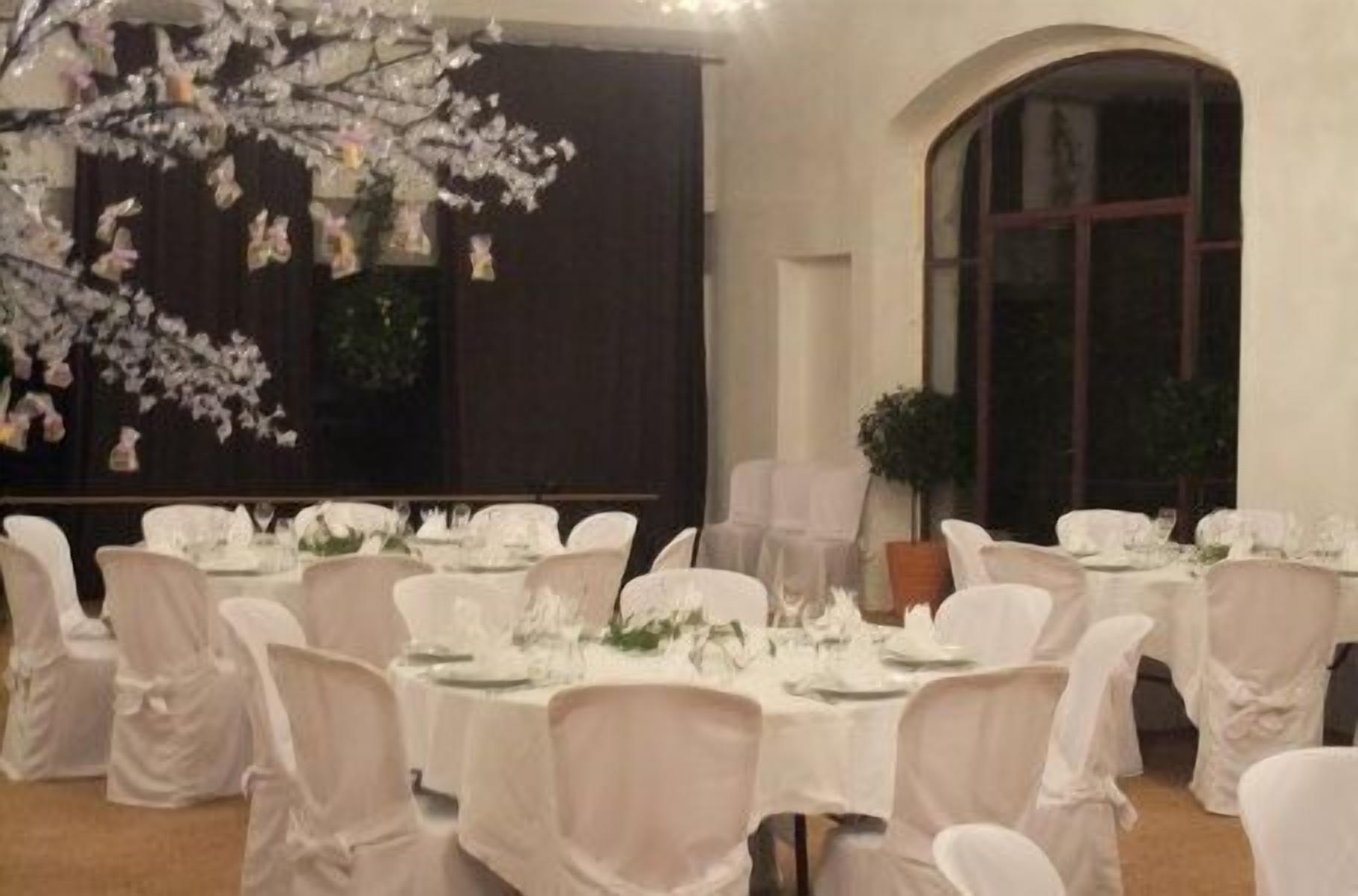Un salón de banquetes con mesas redondas cubiertas con manteles blancos, sillas blancas y decoraciones florales en las paredes.