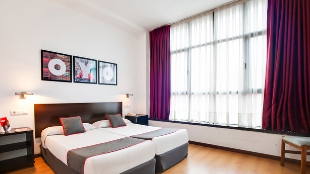 A double bed with a headboard, two bedside tables, a nightstand, a window with curtains, and wall art. - Parque Empresarial by Vivere Stays (Aviles)