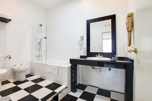 Un baño con suelo a cuadros blanco y negro, una bañera, un lavabo con espejo y un inodoro.