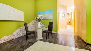 A lobby with a green wall, a glass-top table with two chairs, a vase with flowers, and a painting of a landscape. - Parque Empresarial by Vivere Stays (Aviles)
