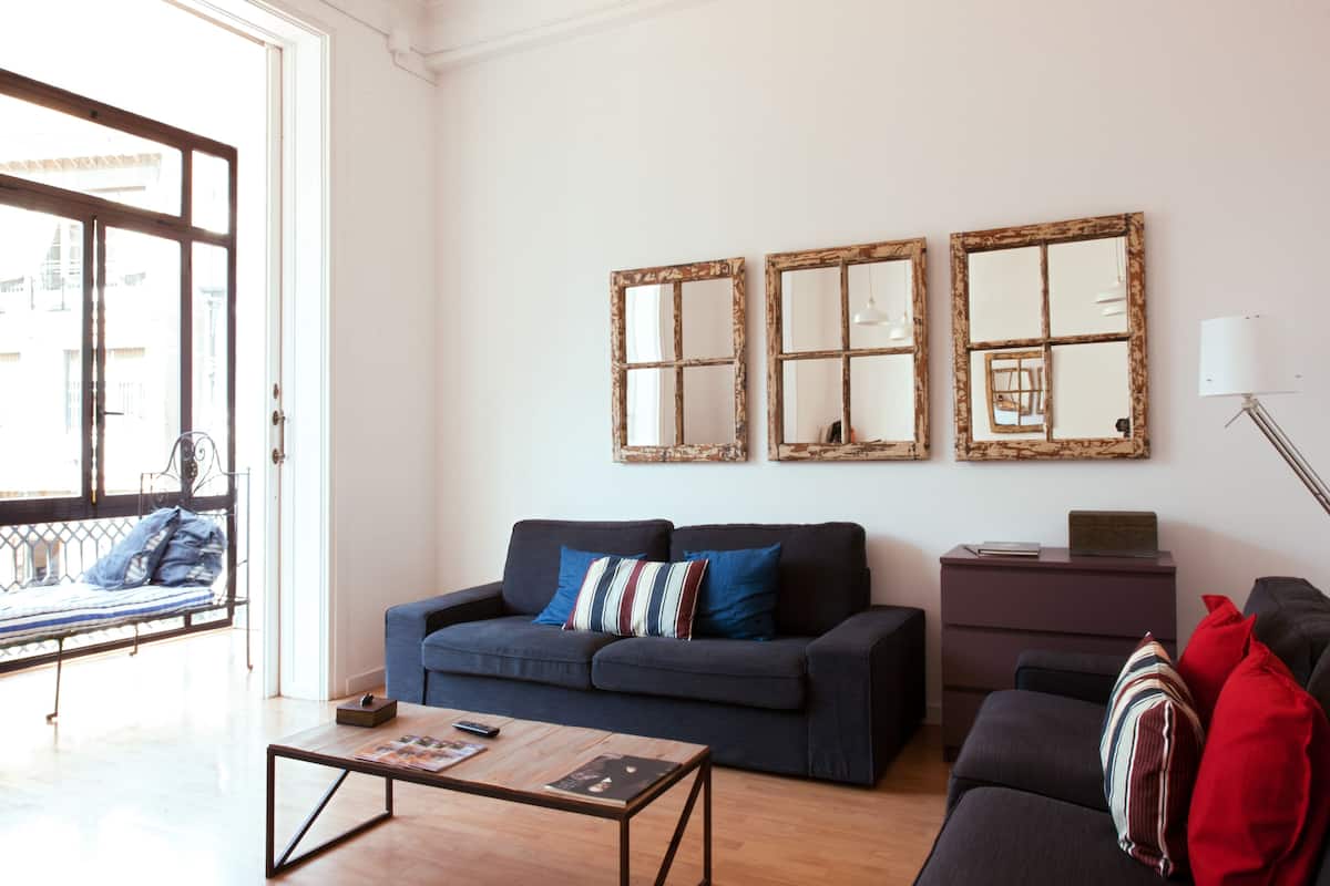 A living room with a sofa, a coffee table, and a side table. There are three large mirrors on the wall.