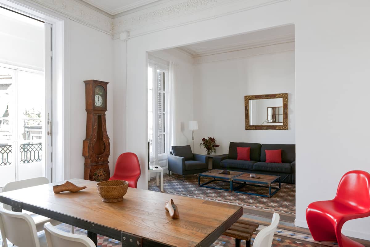 A room with a wooden dining table, red and white chairs, a sofa, and a large mirror on the wall.