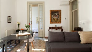 A living room with a sofa, a dining table with chairs, a painting on the wall, and a door leading to another room. - My Address in Barcelona (Barcelona)