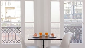 A table with two plates of croissants and two glasses of orange juice, set between two white chairs, with a view of a balcony and buildings through large windows. - My Address in Barcelona (Barcelona)