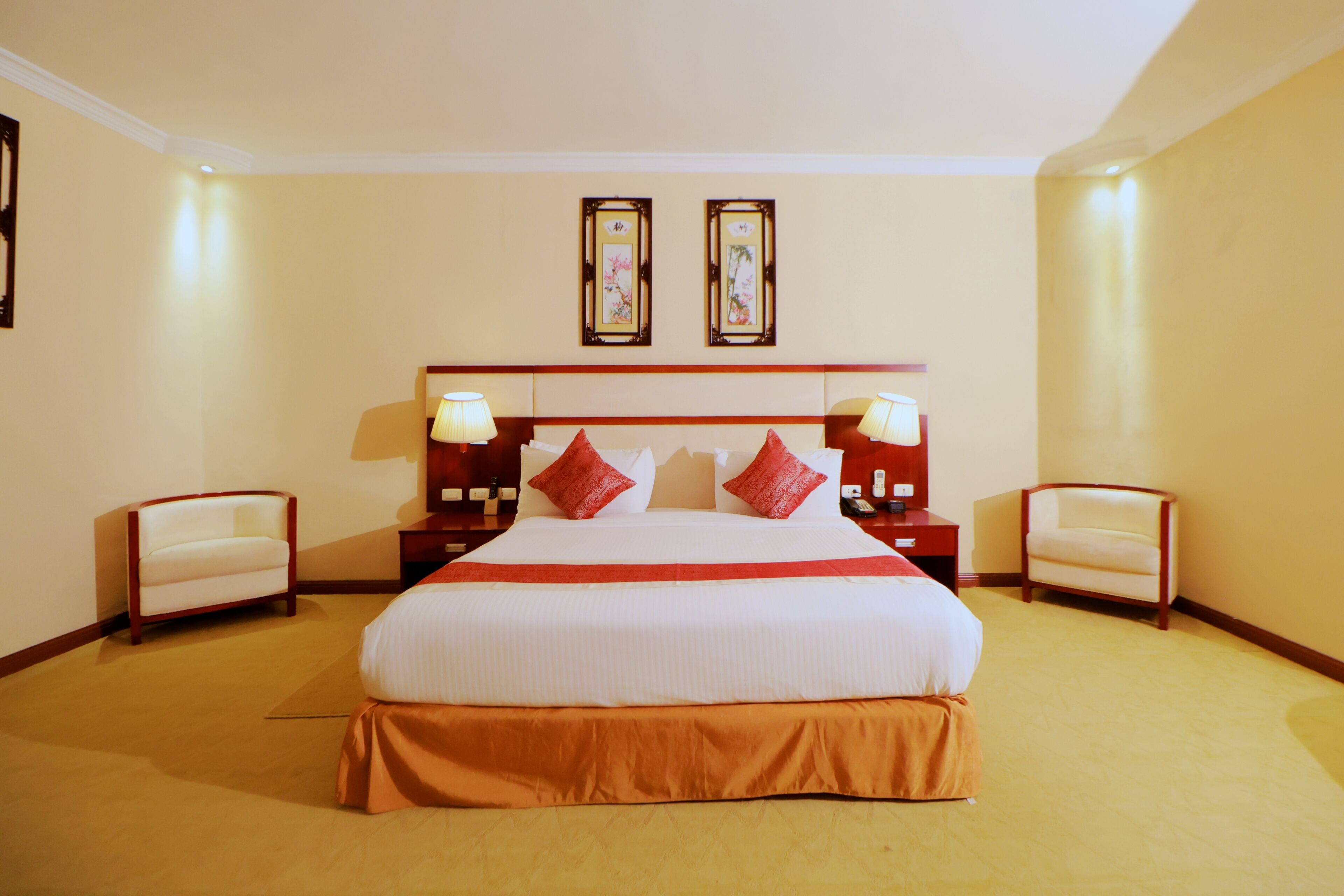 Een hotelkamer met een groot bed, twee nachtkastjes met lampen, een stoel en twee ingelijste foto's aan de muur.