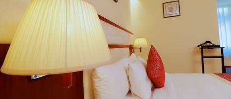 A hotel room with a bed, a large wall-mounted lamp, a bedside table, a chair, and a framed picture on the wall.