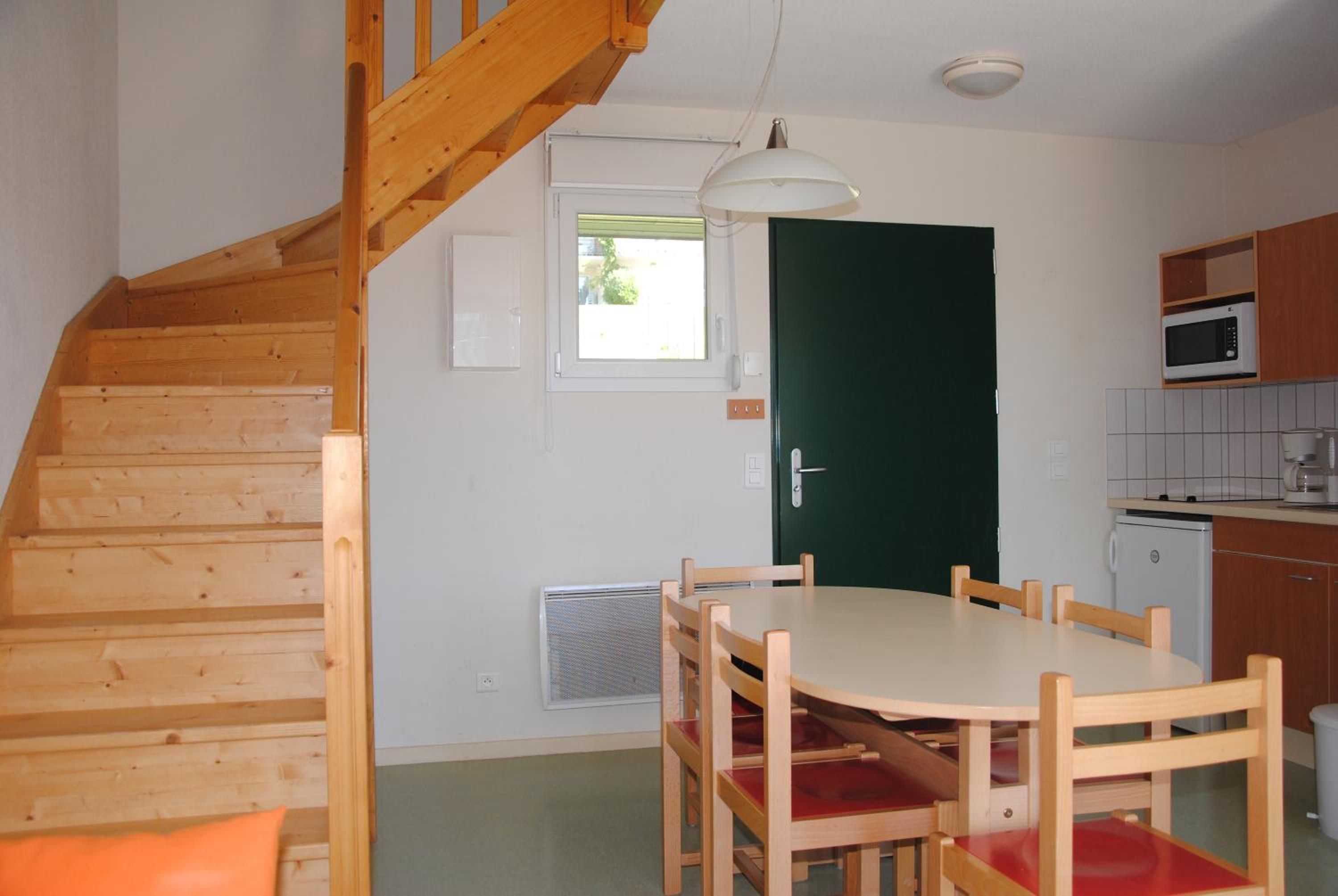 Une cuisine compacte avec un coin repas, un escalier en bois et une porte verte.