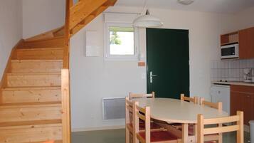 A compact kitchen with a dining area, wooden staircase, and a green door.