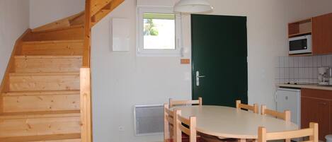 A compact kitchen with a dining area, wooden staircase, and a green door.