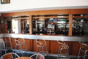 Uma área de bar com balcão, banquetas e prateleiras cheias de garrafas.