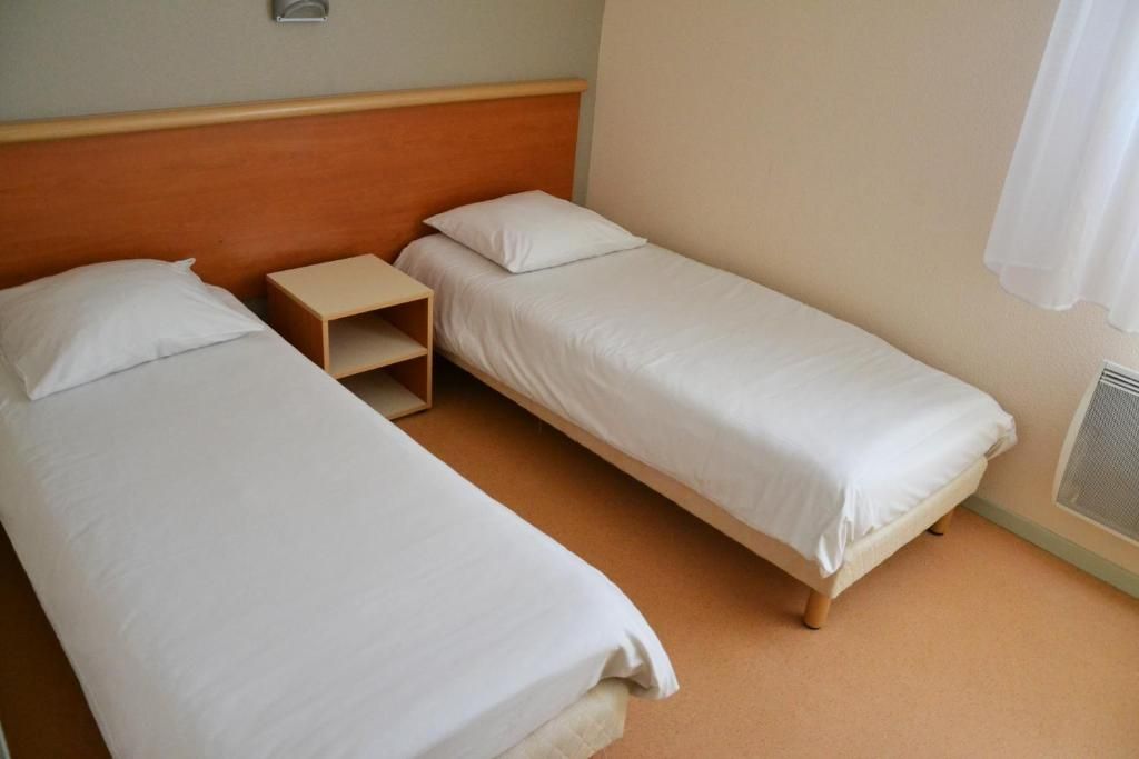 Habitación doble con dos camas individuales, una mesita de noche de madera y una ventana con cortina blanca.