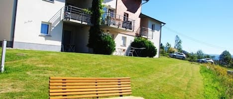 Een tweelaags gebouw met een balkon en een gazon met een houten bank.