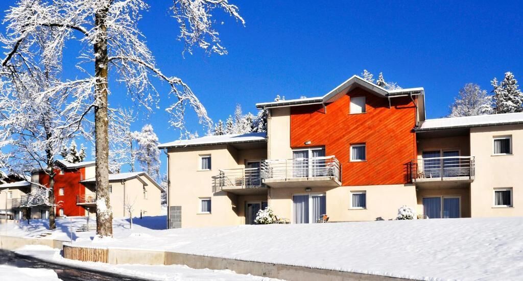 Un edificio de varios pisos con balcones, un paisaje nevado y cielos azules despejados.