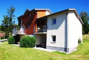 Une maison moderne à deux étages, dotée d’un balcon, d’un petit patio et d’une pelouse bien entretenue.