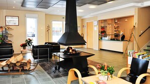 A lobby with a fireplace, seating area, and a reception desk. - Résidence Le Herbau (Gerardmer)